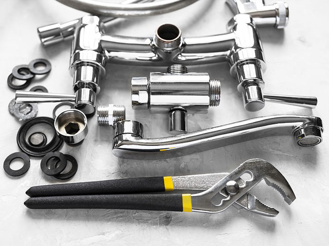 Polished chrome kitchen sink faucet parts disassembled with a wrench